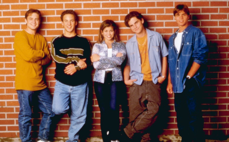 Пятеро подростков в повседневной одежде 90-х, прислонившись спиной к кирпичной стене и улыбаясь;  рекламное изображение для 