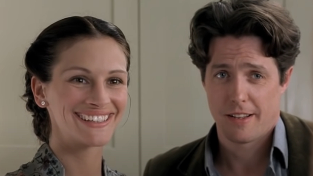 Julia Roberts and Hugh Grant stand smiling together in Notting Hill.