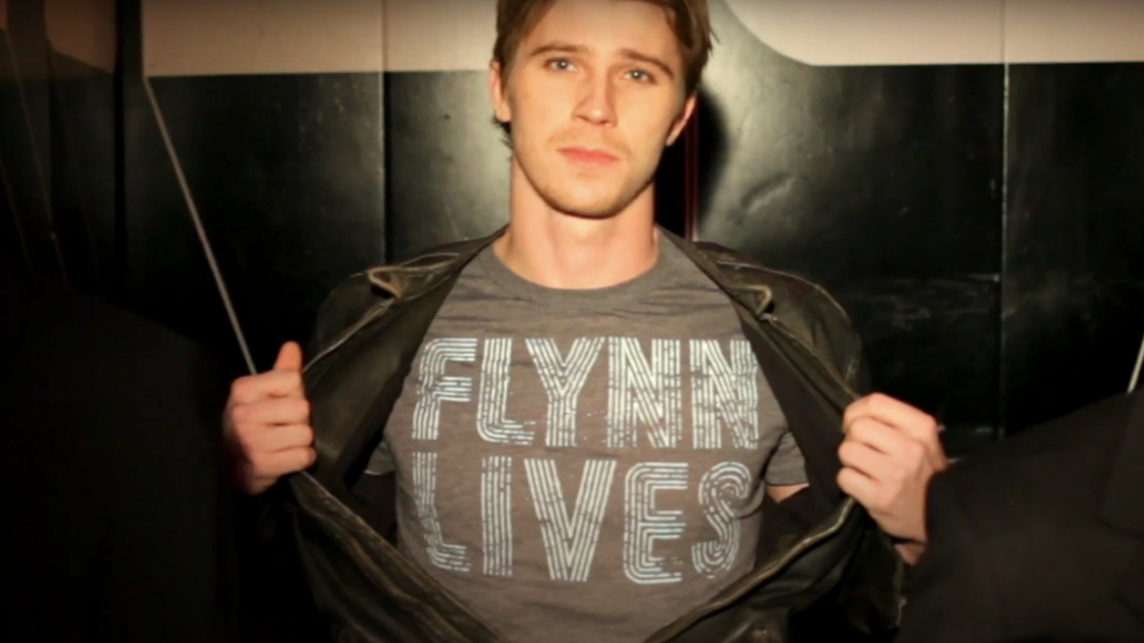 Гаррет Хедлунд демонстративно демонстрирует перед камерой свою футболку Flynn Lives в фильме «Трон: Следующий день».