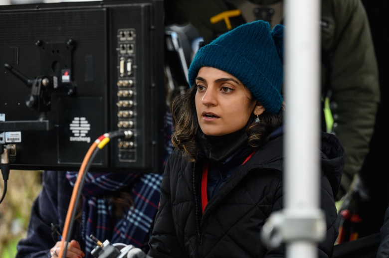 Женщина в пальто и шляпе смотрит видеомонитор на съемочной площадке;  закулисное фото режиссера Ниды Манзур на 