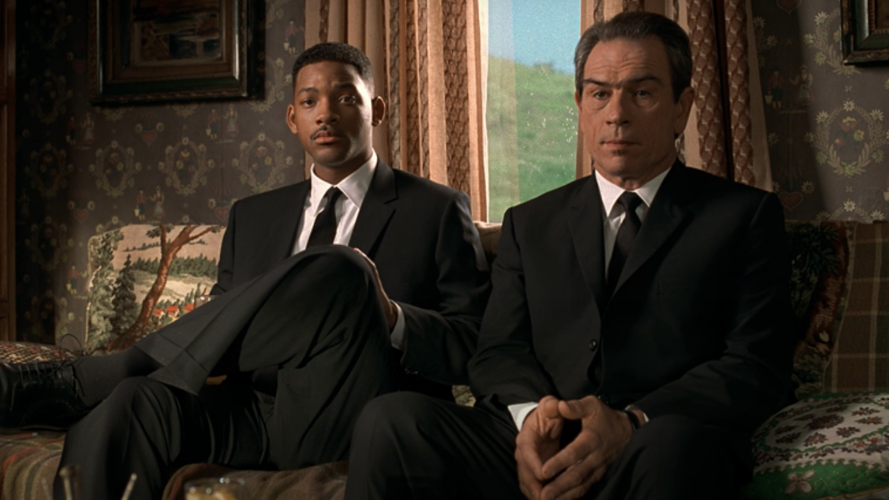 Will Smith et Tommy Lee Jones patiemment assis sur un canapé, écoutant une histoire dans Men in Black.