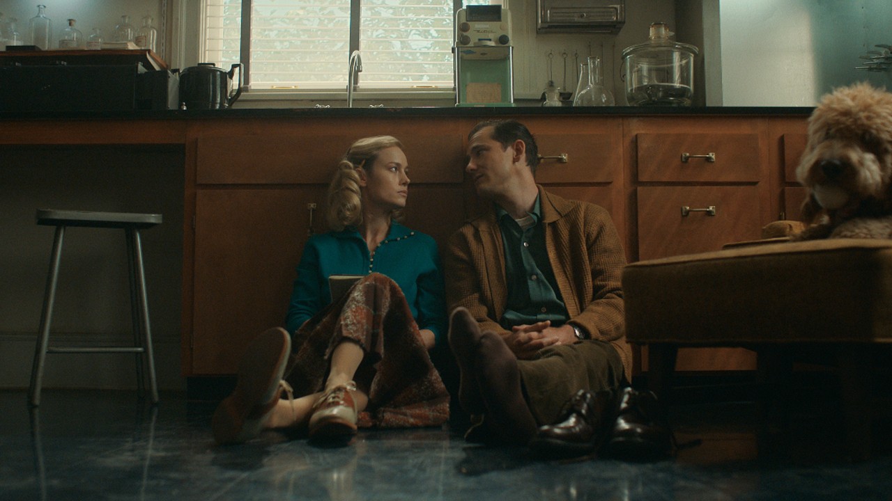 Ein Pressefoto von Lessons in Chemistry von Brie Larson und Lewis Pullman, die auf dem Boden sitzen.