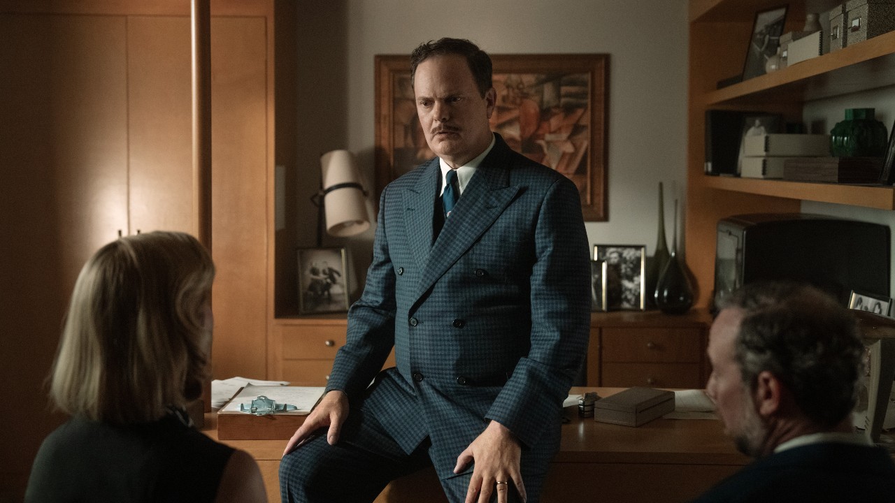Pressebild von Rainn Wilson als Phil in Lessons in Chemistry, wie er an seinem Schreibtisch lehnt und mit Elizabeth und Walter spricht.