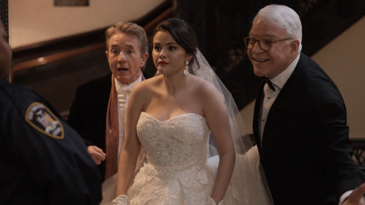 Ein Screenshot von „Only Murders in the Building“ von Selena Gomez in einem Hochzeitskleid, mit Steve Martin zu ihrer Rechten lächelnd und Martin Short hinter ihr, der etwas schockiert aussieht.
