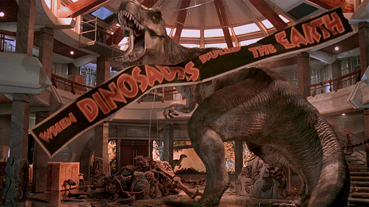 Roberta le T-Rex rugit de façon triomphale, alors qu'une bannière tombe, dans Jurassic Park.