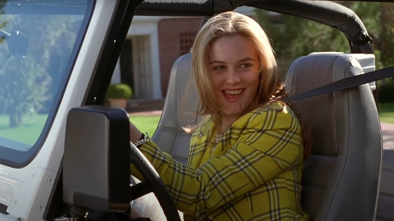 Alicia Silverstone lächelt, während sie in Clueless am Steuer ihres Jeeps sitzt.