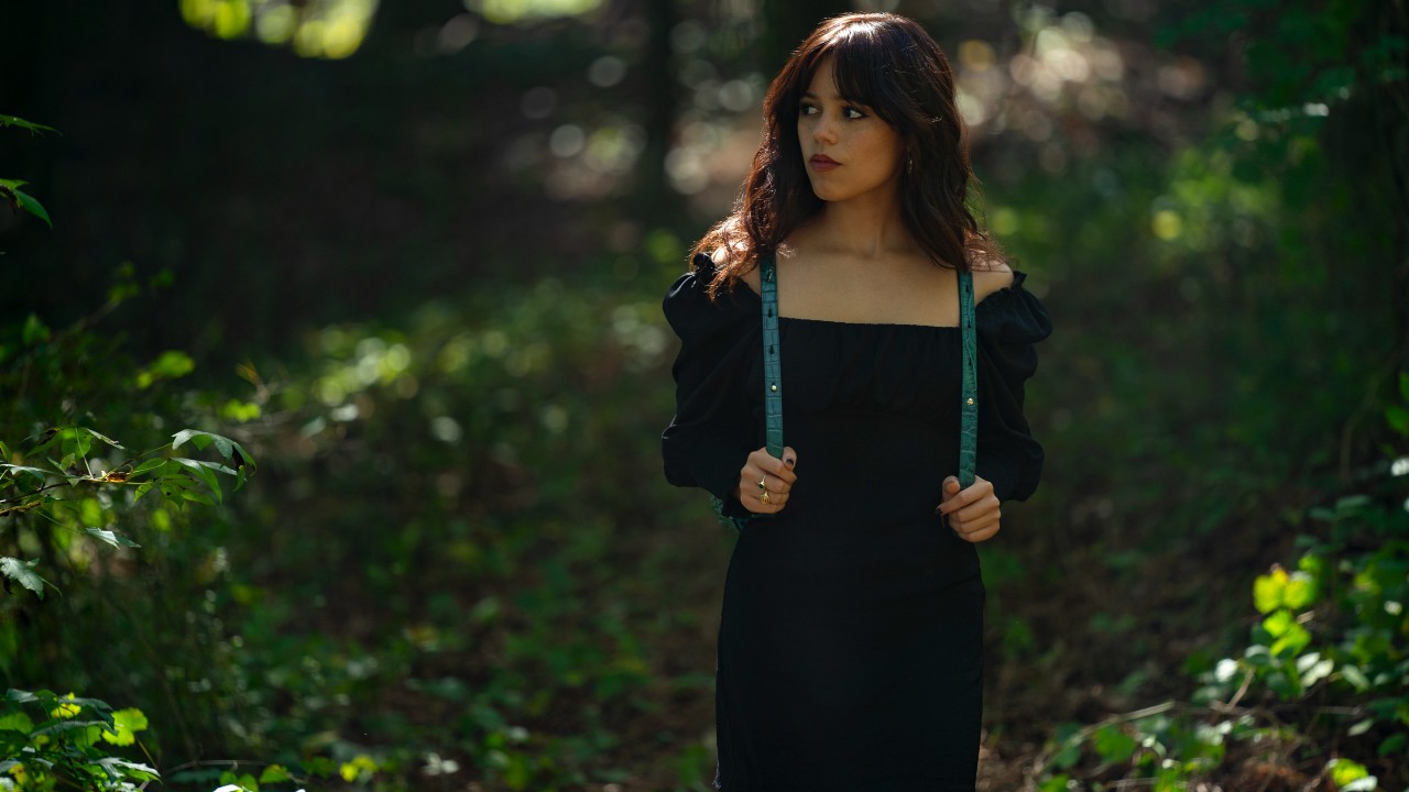 Ein Pressefoto von Jenna Ortega, die in „Miller's Girl“ mit den Trägern ihres Rucksacks durch den Wald läuft.