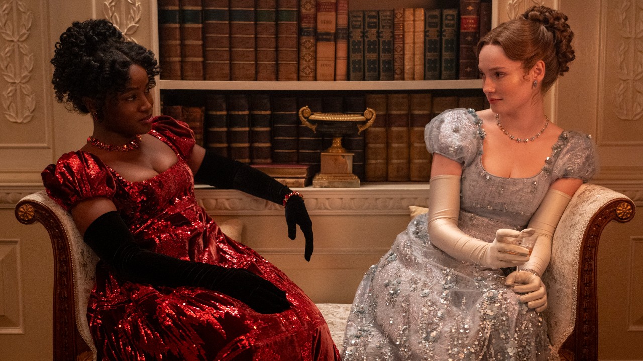 De gauche à droite) Masali Baduza dans le rôle de Michaela, Hannah Dodd dans le rôle de Francesca Bridgerton assise sur un canapé et se regardant.