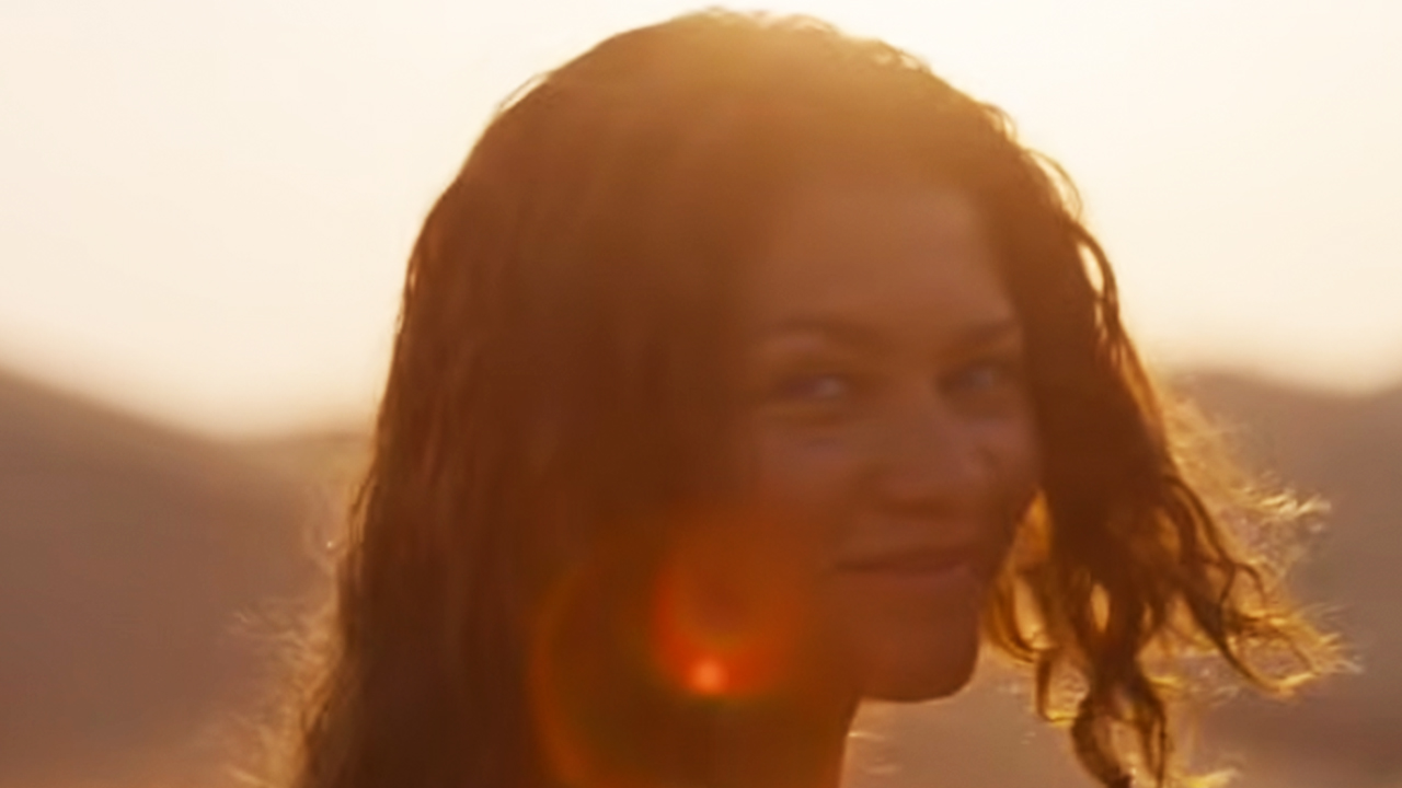 Zendaya regarde en arrière et sourit avec le soleil derrière elle.