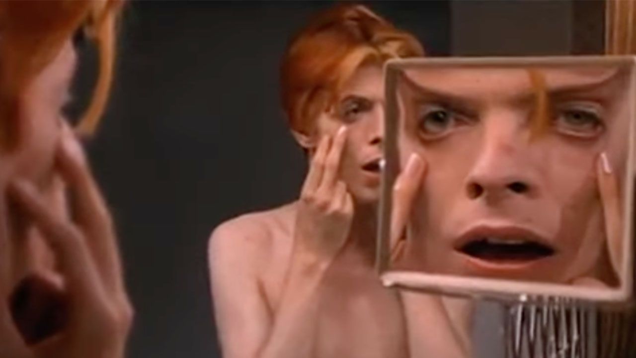 David Bowie betrachtet sich im Spiegel und berührt sein Gesicht in „Man Who Fell to Earth“.