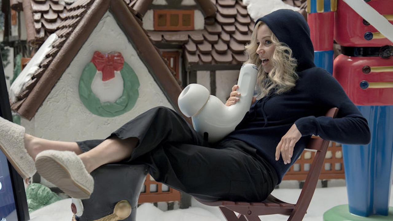 Elizabeth Banks en sweat à capuche parlant sur un airpod dans The Miniature Wife
