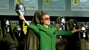 Robert Downey Jr. monte sur scène au Comic-Con dans un costume de Victor Doom, tenant son masque vers le ciel dans un geste triomphal