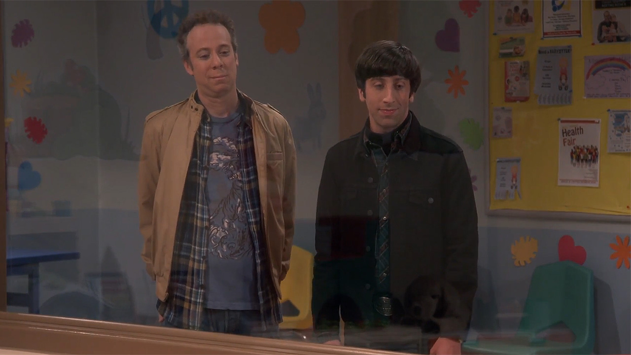 Скриншот Говарда и Стюарта, смотрящих через окно в детский сад на TBBT. На Говарде темная куртка, а на Стюарте светло-коричневое пальто.